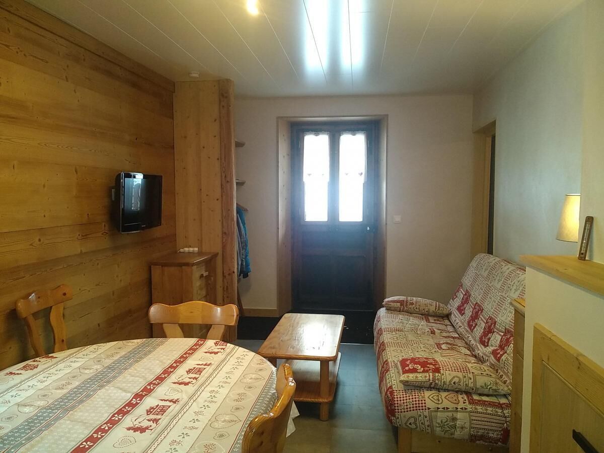 A cozy room with wooden walls, a bed, a sofa, a table, and a TV.