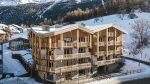 A multi-story wooden building with balconies, set against a snowy mountain backdrop. - Wifi, 50m from ski slopes, fitness, swimming pool, sauna, hammam, balcony, fireplace or stove, tv (Val Cenis)