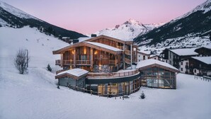 A large, multi-story lodge with wooden exterior and glass windows, surrounded by snow-covered mountains. - Wifi, 50m from ski slopes, fitness, swimming pool, sauna, hammam, balcony, fireplace or stove, tv (Val Cenis)