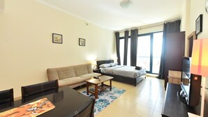 Una sala de estar moderna y bien iluminada con un sofá, una mesa de comedor y una cama. Hay dos cuadros en la pared, un televisor y una lámpara sobre una mesita.