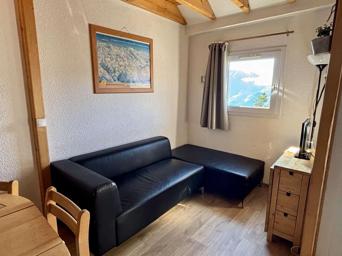 Ein gemütliches Zimmer mit einem schwarzen Sofa, einem Holzesstisch und einem fenster mit Vorhängen.