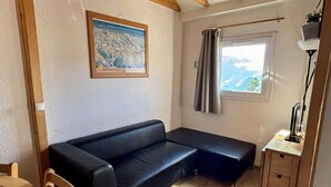 A cozy room with a black sofa, a wooden dining table, and a window with curtains. - 300m from ski lifts, 3rd floor, balcony, tv, ski locker, 31m², Alpe d'Huez (L'Alpe d'Huez)