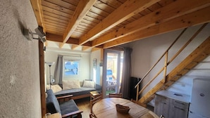 A cozy room with a wooden ceiling, a dining table with chairs, a sofa, and a kitchen area with a refrigerator. - 300m from ski lifts, 3rd floor, balcony, tv, ski locker, 31m², Alpe d'Huez (L'Alpe d'Huez)
