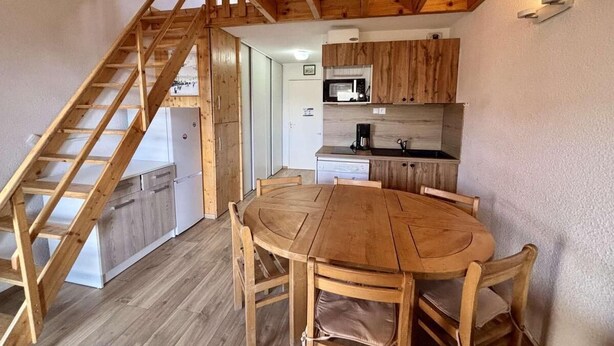A wooden interior with a dining table, chairs, a kitchen area with appliances, and a wooden staircase. - 300m from ski lifts, 3rd floor, balcony, tv, ski locker, 31m², Alpe d'Huez (L'Alpe d'Huez)