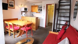 Un espacio habitable compacto con comedor, kitchenette y dormitorio en entrepiso con sofá rojo estampado de lunares.