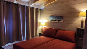 Una habitación acogedora con techo de madera, cama con ropa de cama roja, mesita de noche con lámpara y un cuadro en la pared.