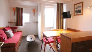 Una habitación acogedora con una cama de madera, una pequeña mesa redonda, una mesa de comedor con sillas y un televisor en la pared.