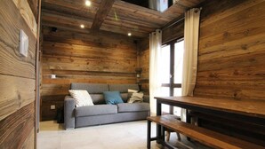 Una habitación acogedora con detalles de madera, un sofá gris con cojines, un banco de madera y una ventana con cortinas.