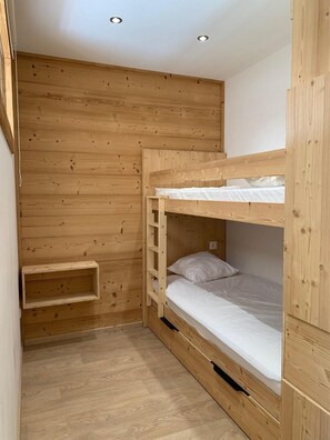 A small, wooden room with a bunk bed, a shelf, and a light switch on the wall. - 10m from resort center, 1st floor, balcony, tv, 35m², Alpe d'Huez (L'Alpe d'Huez)