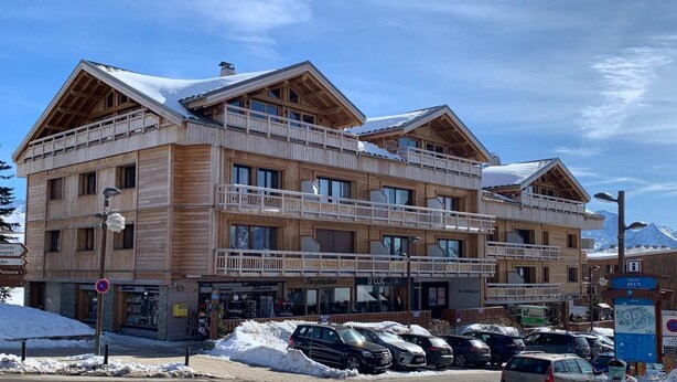 A multi-story wooden building with balconies, a ski lift, and a parking area with cars.