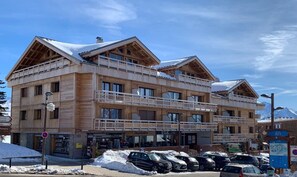 A multi-story wooden building with balconies, a ski lift, and a parking area with cars. - 10m from resort center, 1st floor, balcony, tv, 35m², Alpe d'Huez (L'Alpe d'Huez)