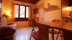 A cozy room with a wooden ceiling, a plaid sofa, a dining table with chairs, a window with curtains, and a small shelf with items. - 5th floor, tv, 16m², Alpe d'Huez (L'Alpe d'Huez)