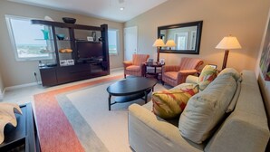 Un salon comprenant un canapé, des fauteuils, une table basse, un téléviseur et une bibliothèque.