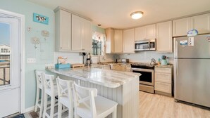 A kitchen with white cabinets, a marble island, white chairs, a stainless steel refrigerator, and a microwave.