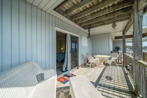 Eine überdachte Terrasse mit Korbmöbeln, eine Schiebetür zu einem Raum und Blick auf das Meer.