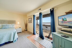 Quarto com cama, mesa de cabeceira, televisão e vista para a varanda.