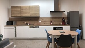 A modern kitchen with white cabinets, a wooden countertop, a built-in microwave, a sink, and a black refrigerator. There is a round table with chairs in the foreground. - 800 M from the basin / direct access to cycle path 6 people (Andernos-les-Bains)