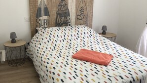 A bedroom with a bed, a headboard with surfboard designs, two bedside tables with lamps, and a wooden floor. - 800 M from the basin / direct access to cycle path 6 people (Andernos-les-Bains)