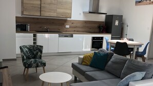 A modern kitchen with wooden cabinets, a dining area with a gray sofa and blue chairs, and a skylight above. - 800 M from the basin / direct access to cycle path 6 people (Andernos-les-Bains)