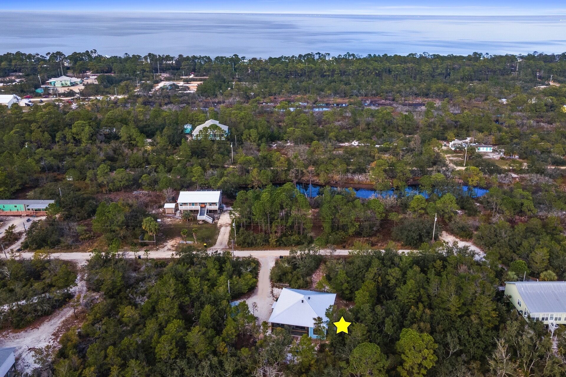 Vista aérea de una zona costera con varios edificios, un bosque denso y una extensión de agua azul.