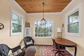 A sunroom with a wooden ceiling, large windows, a dining table, and wicker chairs.