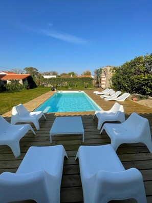 A swimming pool with white lounge chairs and a wooden deck.