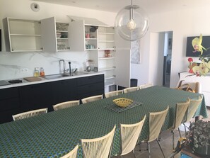 A modern kitchen with white cabinets, a large island with a green patterned tablecloth, and a dining area with wicker chairs.