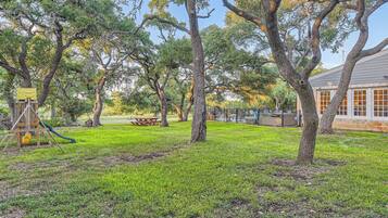 Enjoy a shaded outdoor space with a picnic table and play structure for kids, surrounded by mature trees and a secure fence.