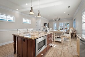 Una cocina amplia con una isla grande, armarios de madera y horno integrado. Hay lámparas colgantes sobre la isla y un comedor con una mesa y sillas.