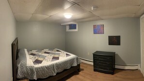 Un dormitorio con cama, cómoda, ventana y dos cuadros en la pared.