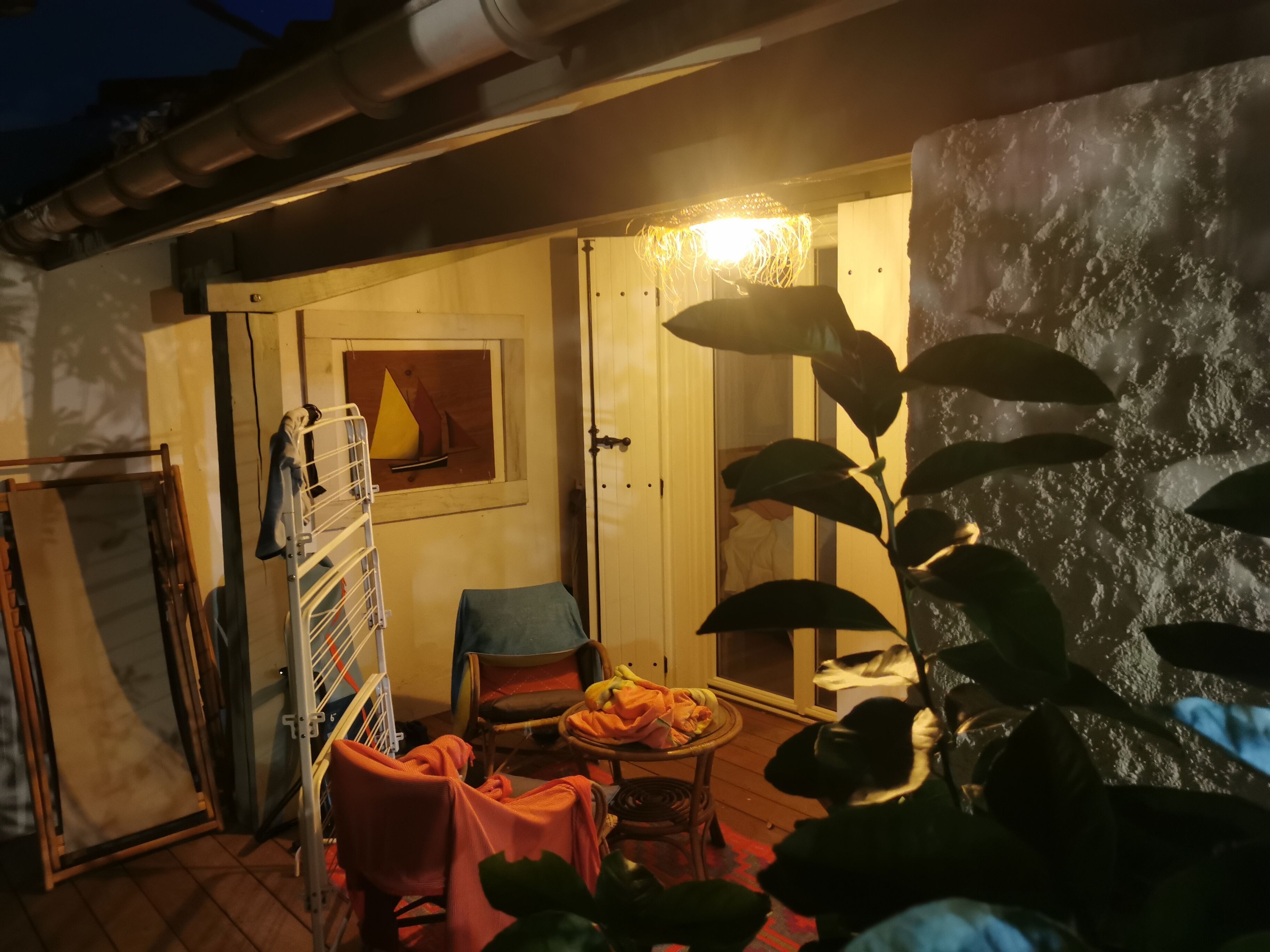 Habitació amb terra de fusta, una cadira, una taula amb llençol i una estanteria penjada a la paret.