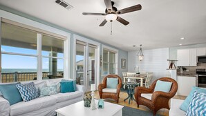 A spacious living room with a white sofa, two wicker chairs, a coffee table, and a view of the ocean through large windows. - Saltwater Breeze- Book 5+ nights & get 15% off -Beach Front-3BD/2BA. Sleeps 9 (Galveston)