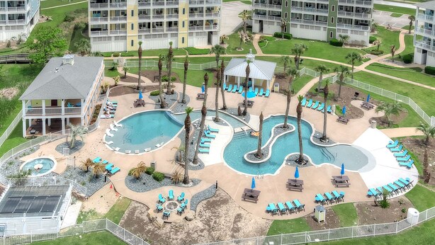 An aerial view of a resort with multiple buildings, a central pool area with multiple water features, and outdoor seating areas. - Saltwater Breeze- Book 5+ nights & get 15% off -Beach Front-3BD/2BA. Sleeps 9 (Galveston)
