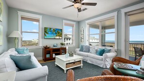 A spacious living room with a view of the ocean, featuring a white sofa, a white coffee table, and wicker chairs. - Saltwater Breeze- Book 5+ nights & get 15% off -Beach Front-3BD/2BA. Sleeps 9 (Galveston)