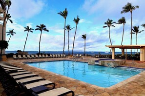 A pool area with lounge chairs, palm trees, and a view of the ocean.