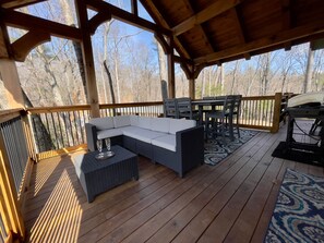 Een overdekt terras met een modulaire bank, eettafel, stoelen en een barbecue.