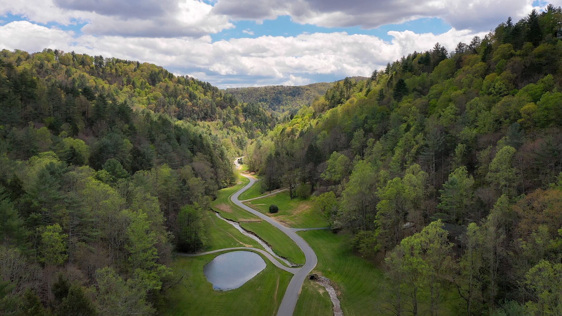 A winding road through a forested valley with a small lake and a clear sky.