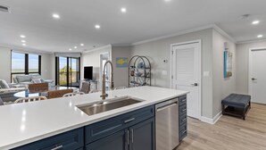 A modern kitchen with a large island, stainless steel appliances, and a dining area with a table and chairs. - Summer House 204 - Pool/Beach - Ocean View! (Isle of Palms)