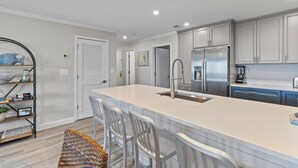 A modern kitchen with white cabinetry, a large island with bar stools, stainless steel appliances, and a built-in sink. - Summer House 204 - Pool/Beach - Ocean View! (Isle of Palms)