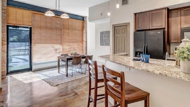 A modern kitchen with dark cabinets, a black refrigerator, and a granite countertop.