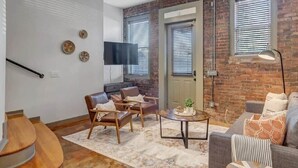 A modern living room with a brick wall, a flat-screen TV, a staircase, and a sofa.