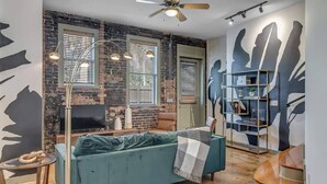 Un salon avec un canapé bleu, un téléviseur, un ventilateur de plafond et une bibliothèque.