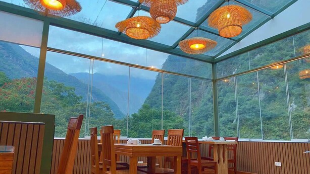 A restaurant with wooden tables and chairs, large windows, and hanging wicker lamps. - Qoya Palace - Machupicchu (Machu Picchu)