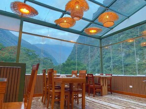 Un restaurant avec des tables et des chaises en bois, de grandes fenêtres et des lampes en osier suspendues au plafond.