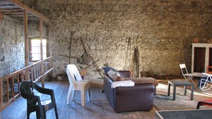 Ein rustikaler Raum mit Steinwand, Holzboden und schlichter Einrichtung, darunter ein Sofa, Stühle und ein Tisch.