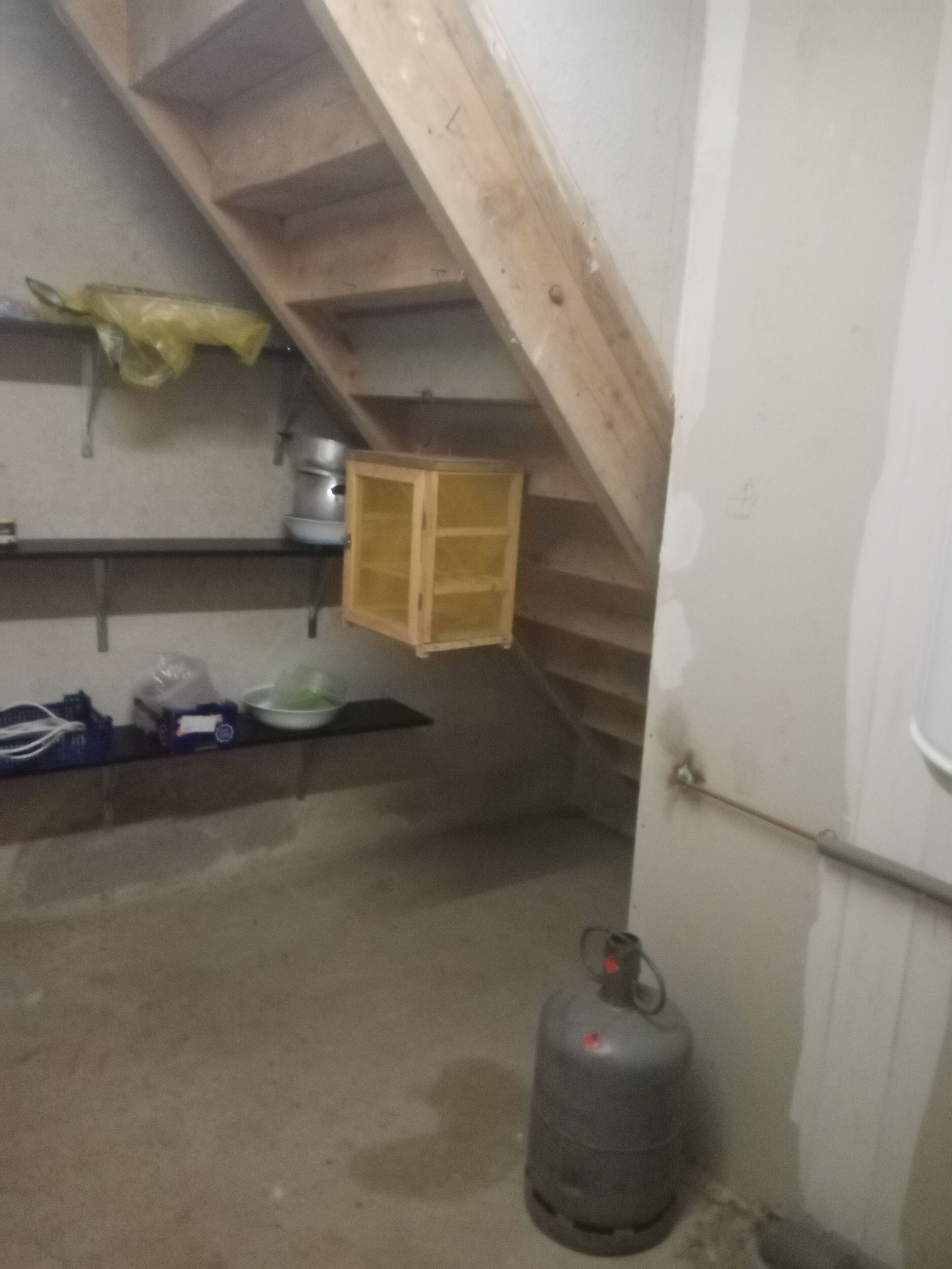 Ett litet, svagt upplyst rum med ett sluttande tak, ett träskåp, en gastub och en dörr.