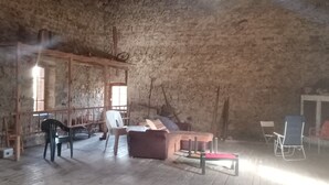Ein Innenraum mit rustikaler Steinwand, Holzbalken, einer Bank und einem Tisch.
