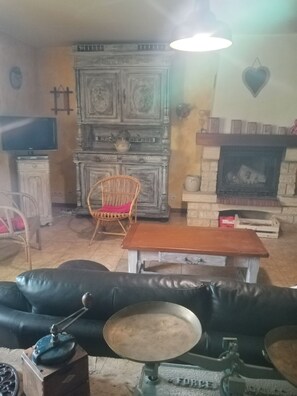 A living room with a fireplace, a television, a wicker chair, and a leather sofa. - Renovated farmhouse with adjoining land (SAINT PAL EN CHALENCON)