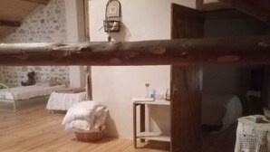 Ein rustikales Dachzimmer mit geneigter Decke, Holzbalken, einer Steinwand und einem kleinen Tisch mit einem Korb und einem weißen Tuch.