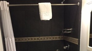 Ein Badezimmer mit Dusche, einer Haltestange, einem Handtuch an der Wand und einem Waschbecken mit Spiegel.